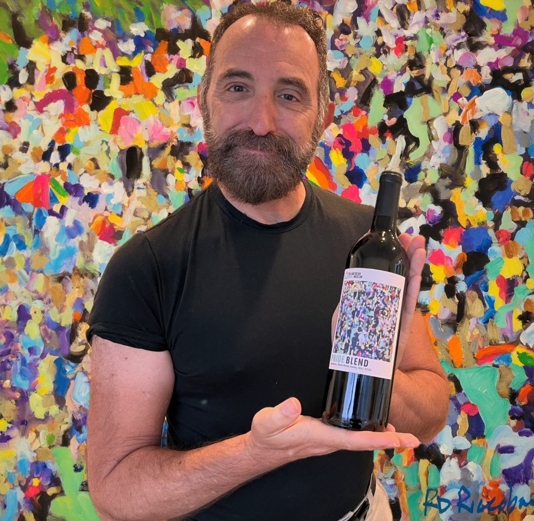 RD Riccoboni holding the American LGBTQ+ Museum Pride Blend wine bottle featuring his painting All That Glitters Is You