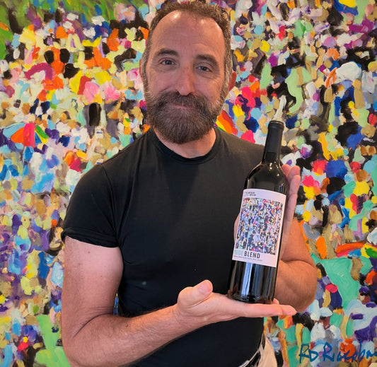RD Riccoboni holding the American LGBTQ+ Museum Pride Blend wine bottle featuring his painting All That Glitters Is You